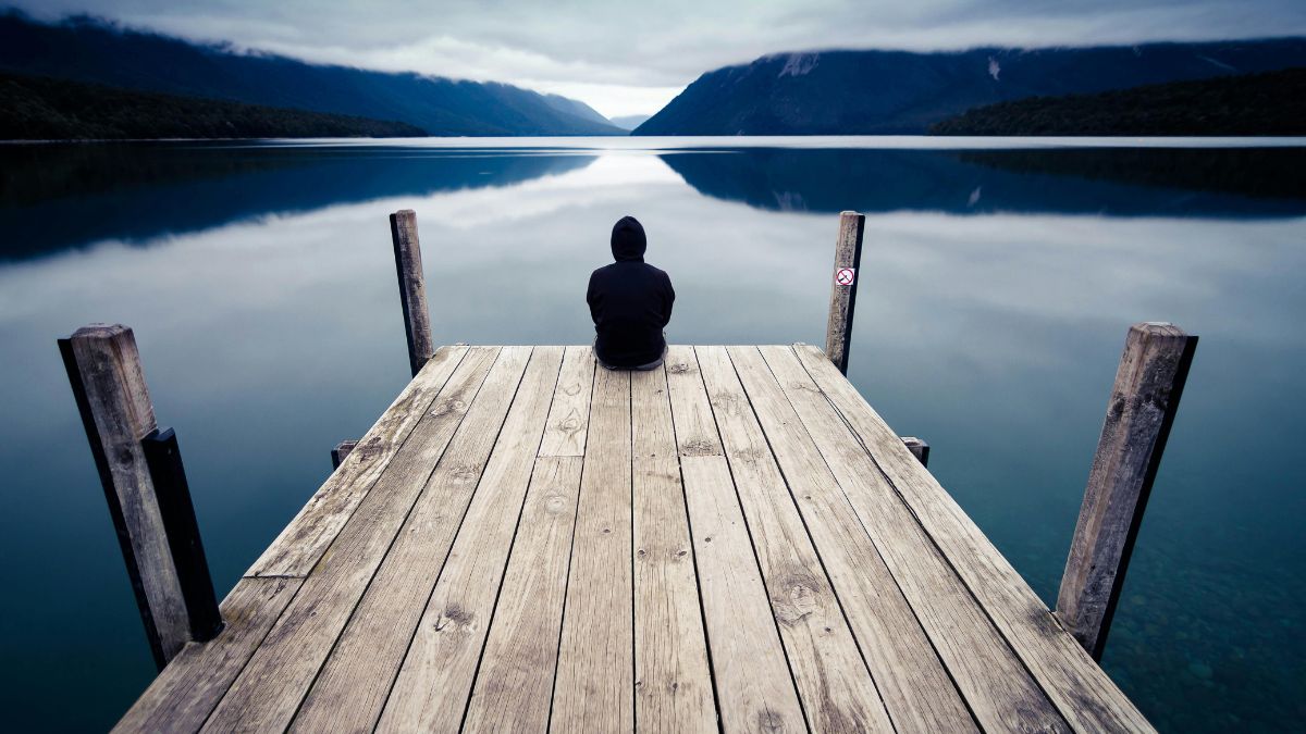 Personne assise seule au bout d'un ponton face à un lac