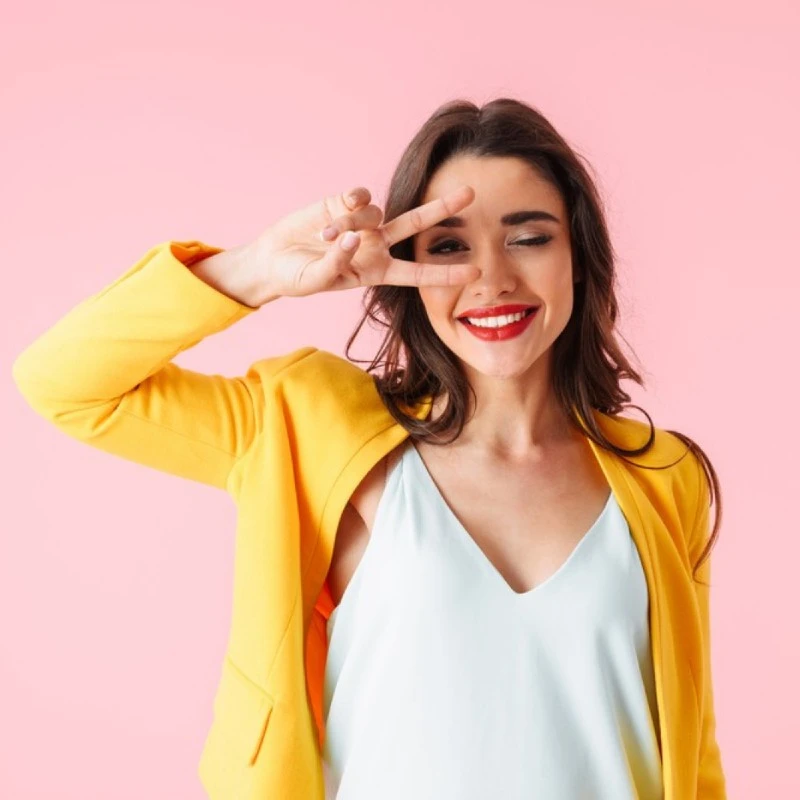 Femme souriante en veste jaune qui fait un signe de la main près de son visage