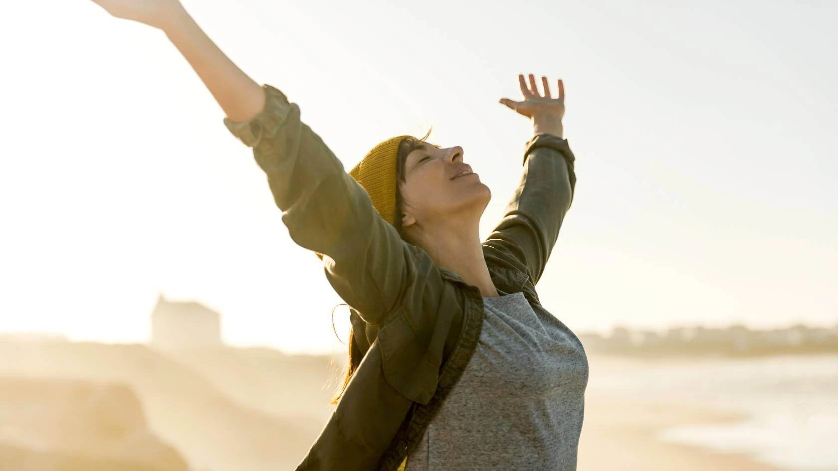 Femme les bras levés face à la mer au soleil, soulagée d'avoir trouvé une reconversion professionnelle qui lui ressemble